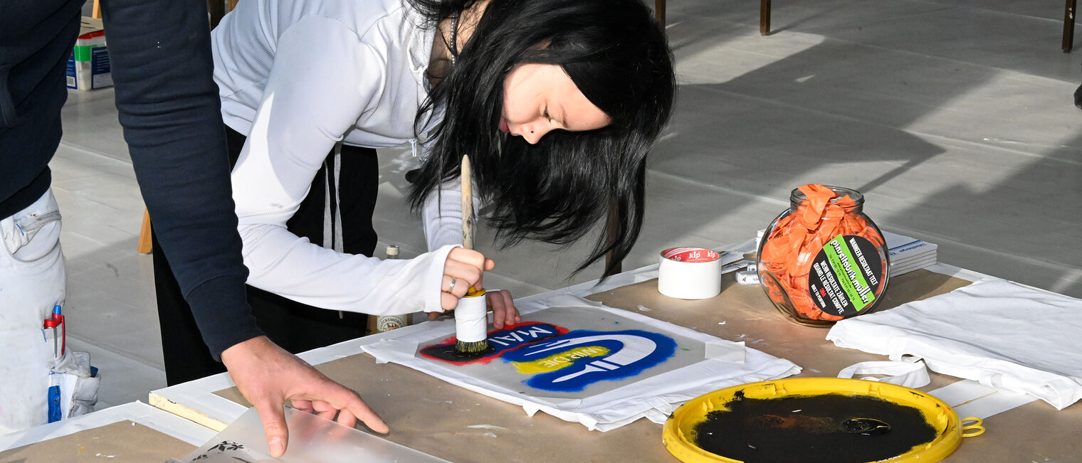 Eine Jugendliche trägt mit einem Pinsel Farbe auf ein Schild auf.