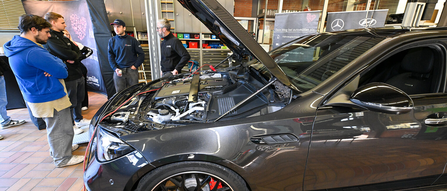 Einige Gäste der Berufsmesse blicken in den Motorraum eines Fahrzeugs.