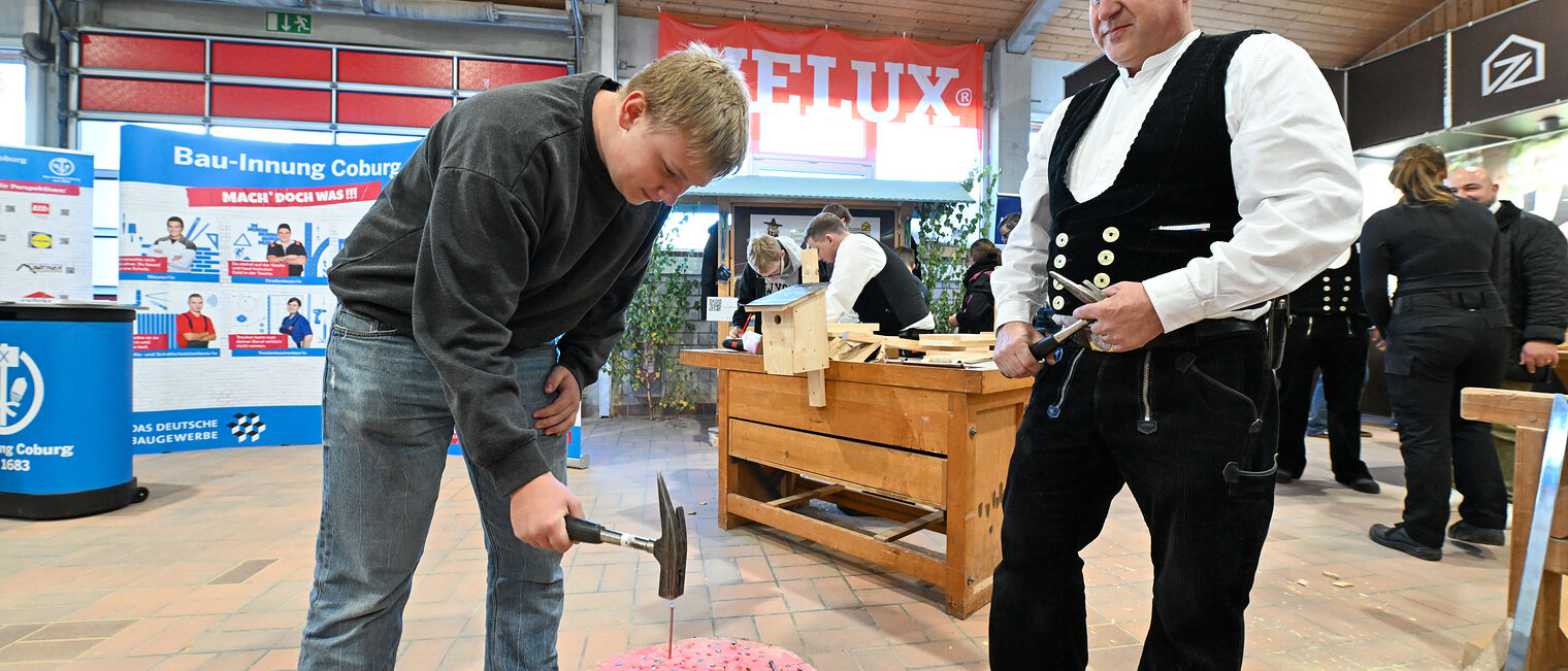 Ein Jugendlicher hämmert unter Beaufsichtigung einen Nagel in einen Baumstumpf. 