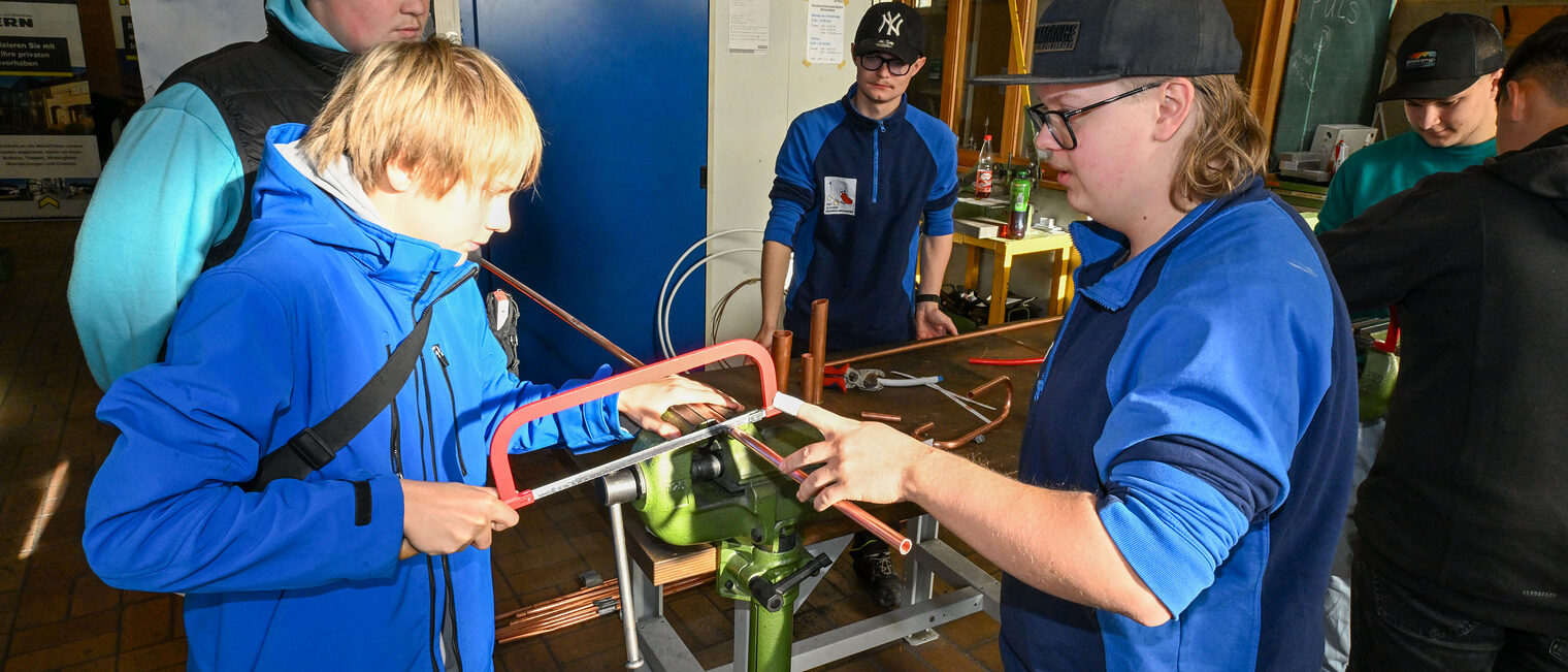 Ein Jugendlicher sägt unter Anleitung ein Metallrohr zurecht.