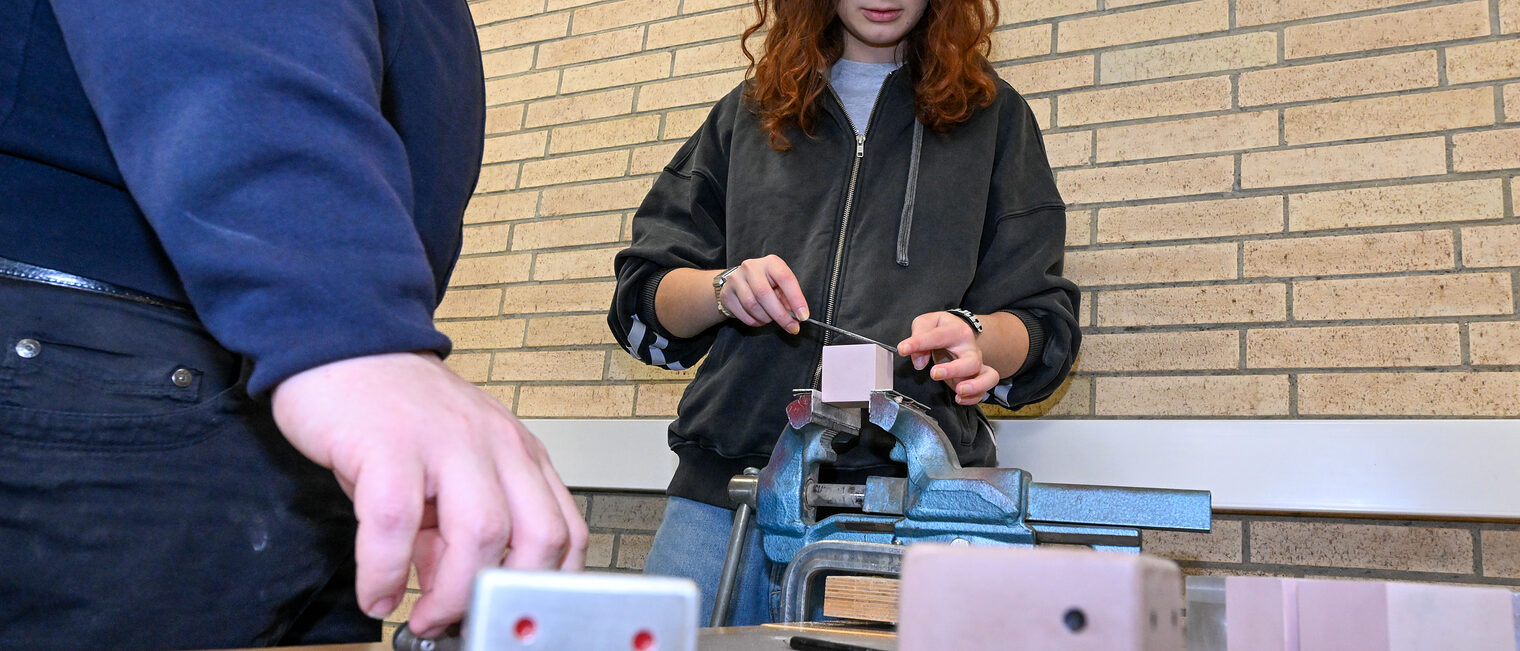 Eine Jugendliche feilt einen Metallwürfel in einem Schraubstock zurecht.