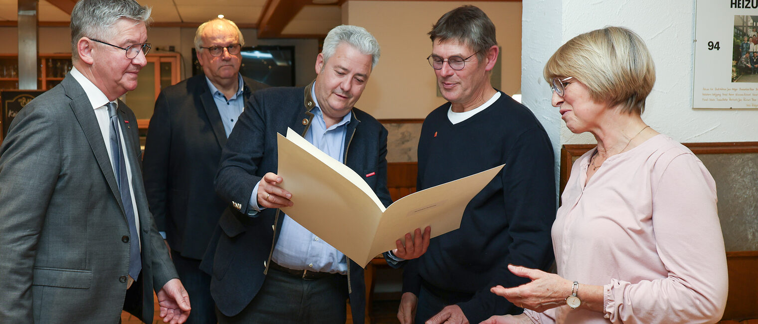 Reinhard Schmidt blickt mit Matthias Graßmann und HWK-Verantwortlichen und seiner Frau auf die Ehrenurkunde