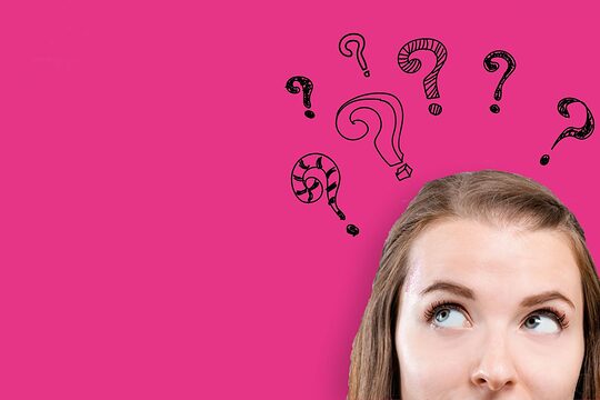 Fragezeichen fliegen um den Kopf einer Frau herum.