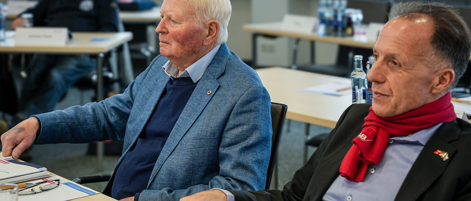 Zwei Vollversammlungsmitglieder hören dem Vortrag zu.