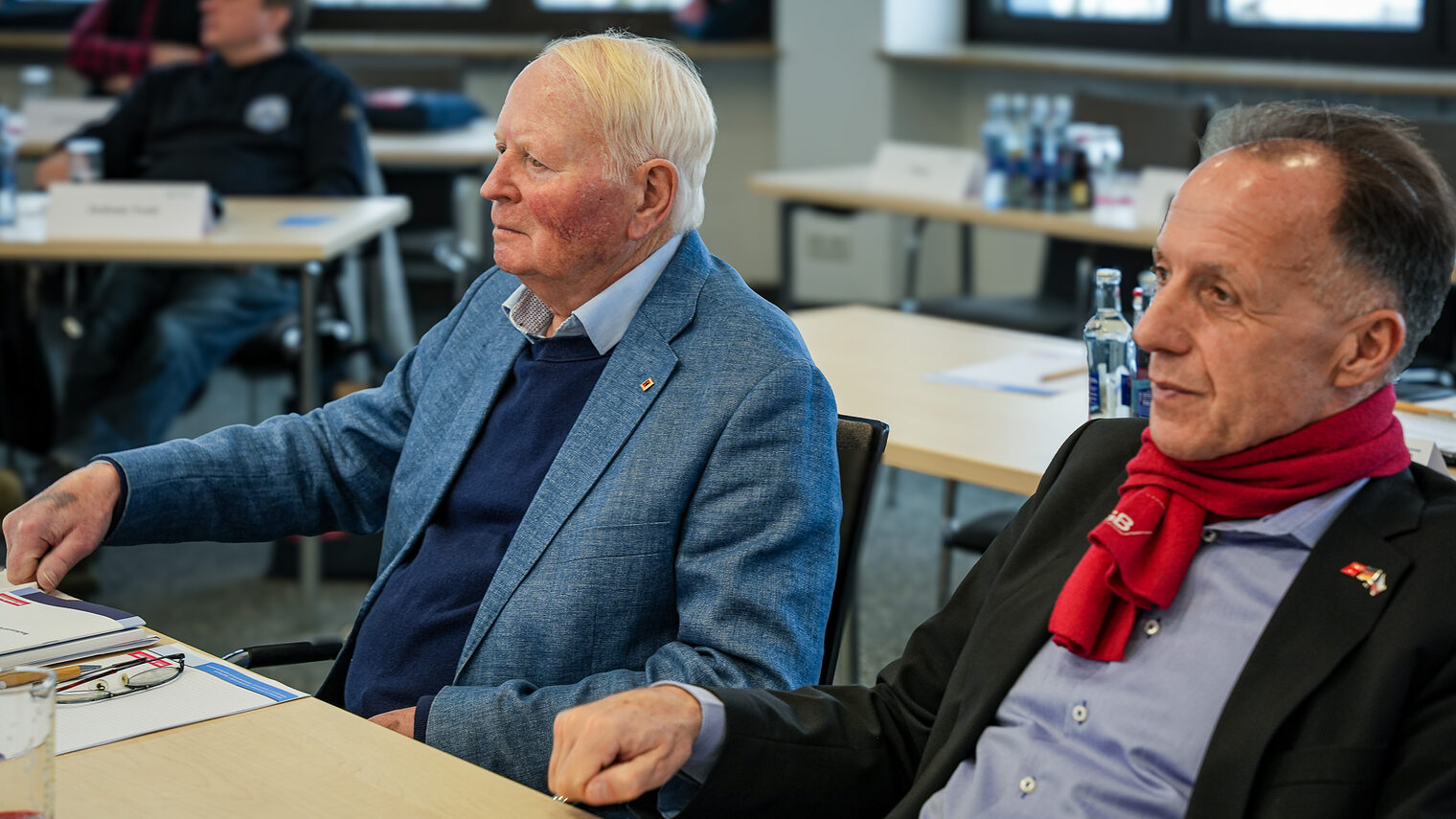 Zwei Vollversammlungsmitglieder hören dem Vortrag zu.