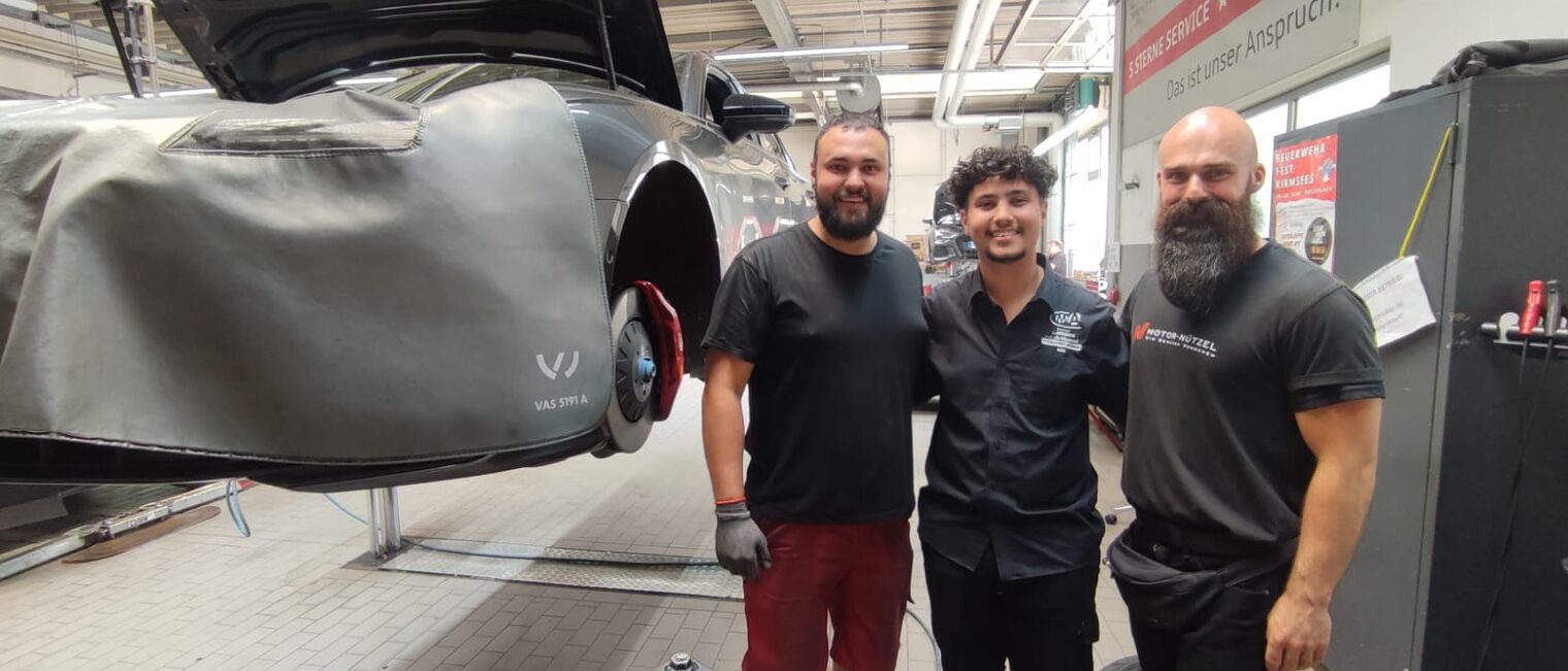 Ein französischer Azubi steht mit den Ausbildungsmeistern in der Werkstatt von Motor Nützel.