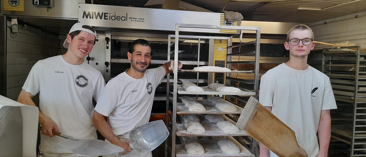 Französische Azubis posieren neben einem Brotwagen mit einem Ausbilder der Bäckerei Feulner. 