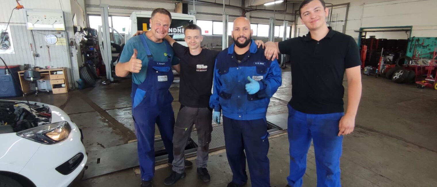 Zwei französische Azubis stehen mit zwei Ausbildern in der Autowerkstatt Gramaglia in Bayreuth.