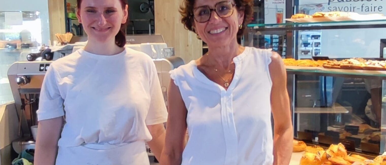 Eine deutsche Azubine steht mit einer Ausbilderin im Verkaufsbereich einer Bäckerei in Lezignan.