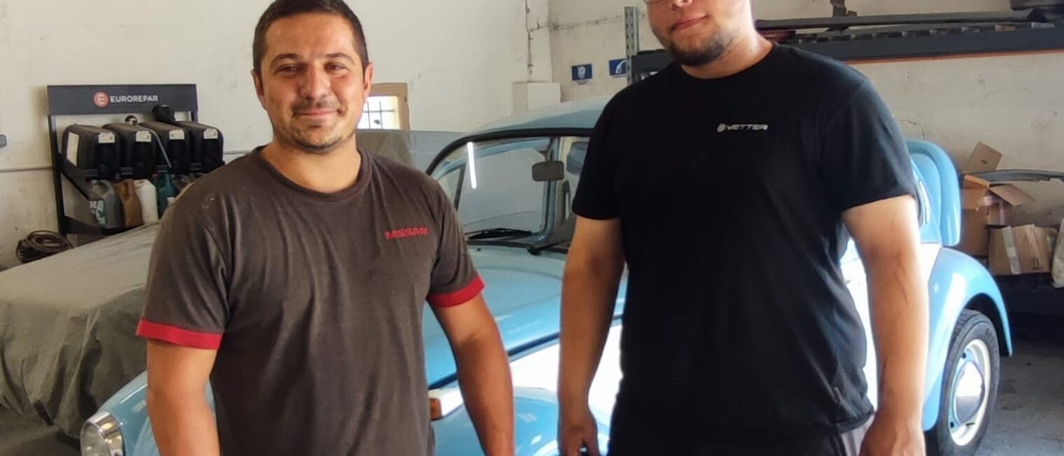 Ein deutscher Azubi steht neben einem Ausbilder und Oldtimer in einer Autowerkstatt in Lezignan.