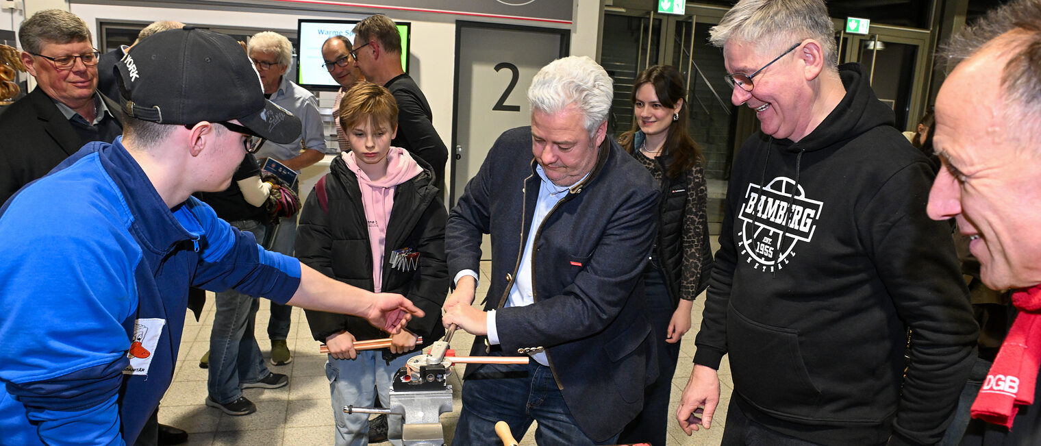 HWK-Präsident Matthias Graßmann biegt unter Aufsicht ein Metallrohr zurecht. 