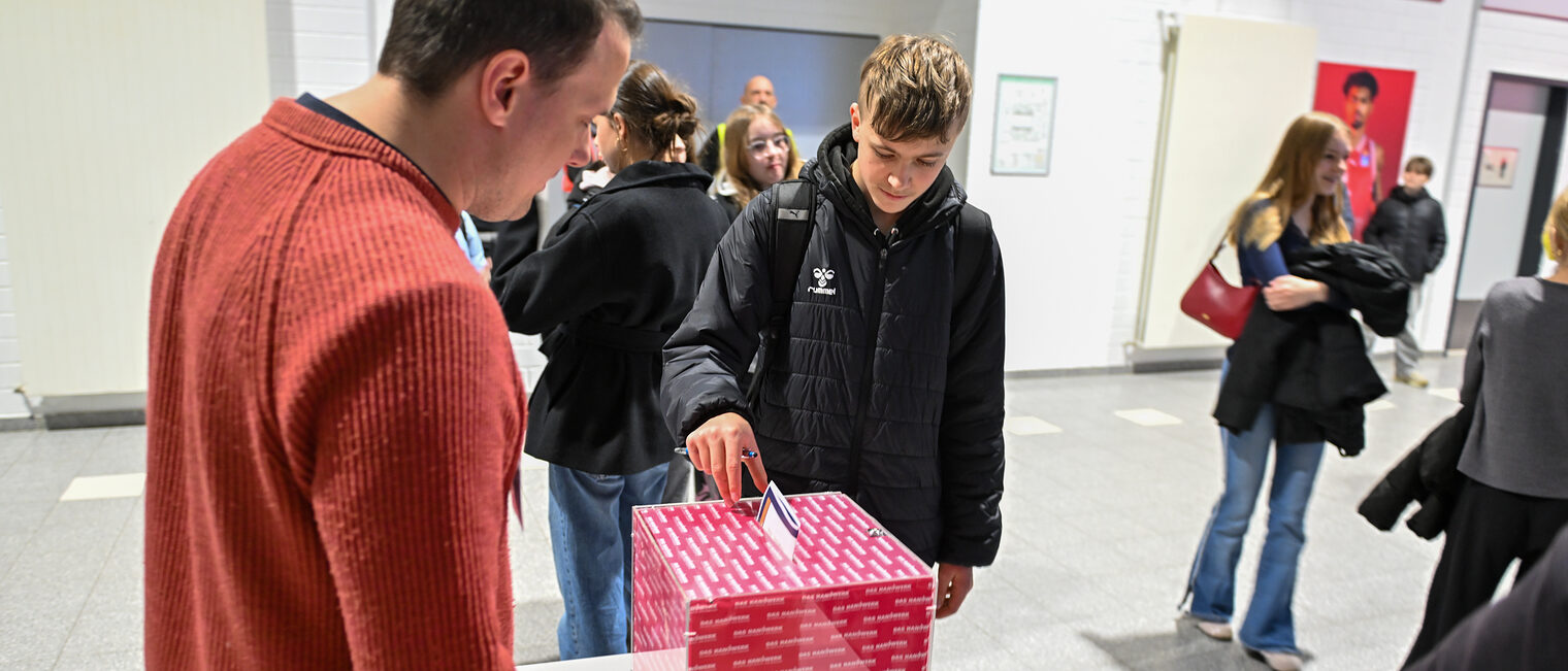 Ein Schüler wirft seine Laufkarte mit seinem Quiz in die Losbox.