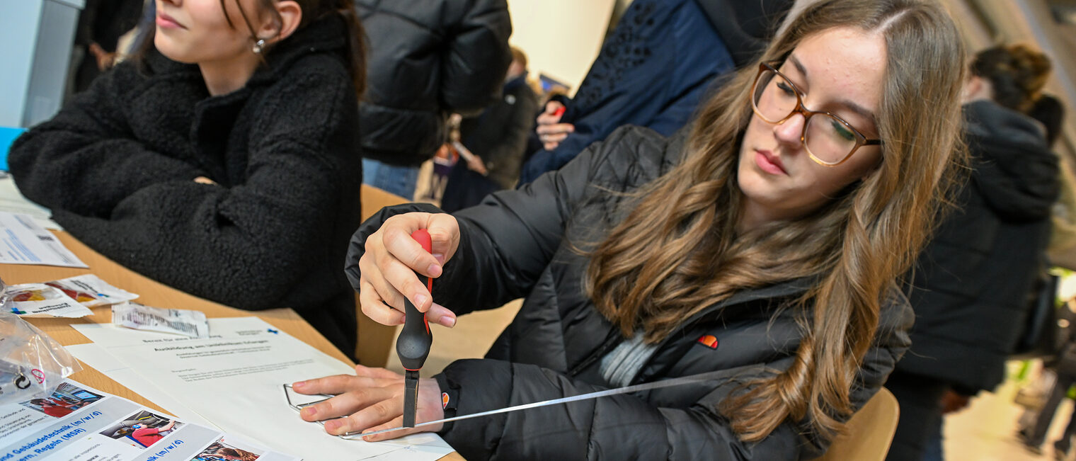 Eine Schülerin zwickt ein Metallrohr mit einer Zange ab.