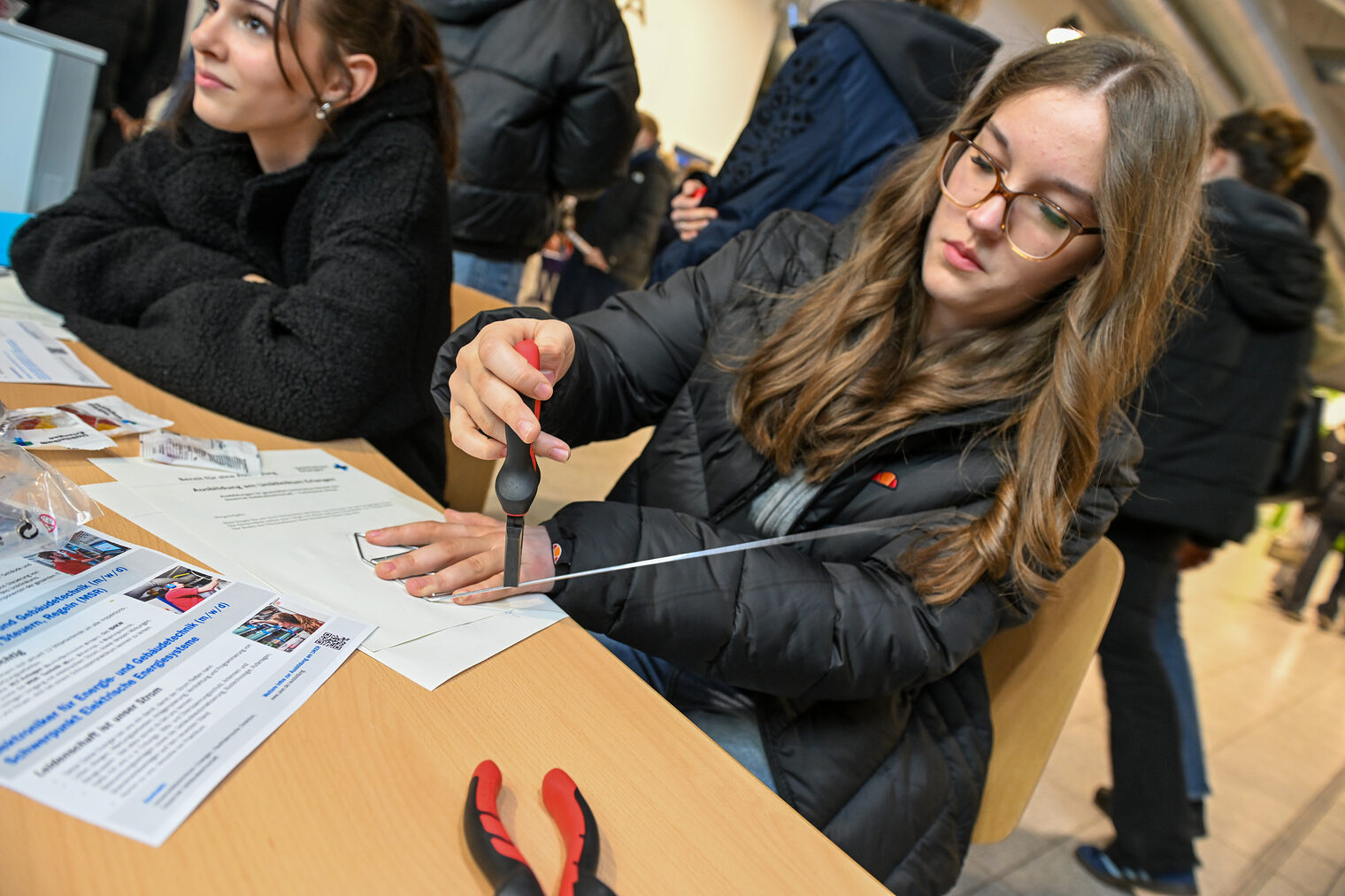 Eine Schülerin zwickt ein Metallrohr mit einer Zange ab.