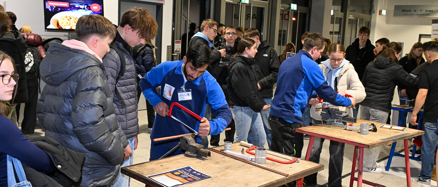 Schülerinnen und Schüler sägen Metallrohre mit Sägen zurecht.