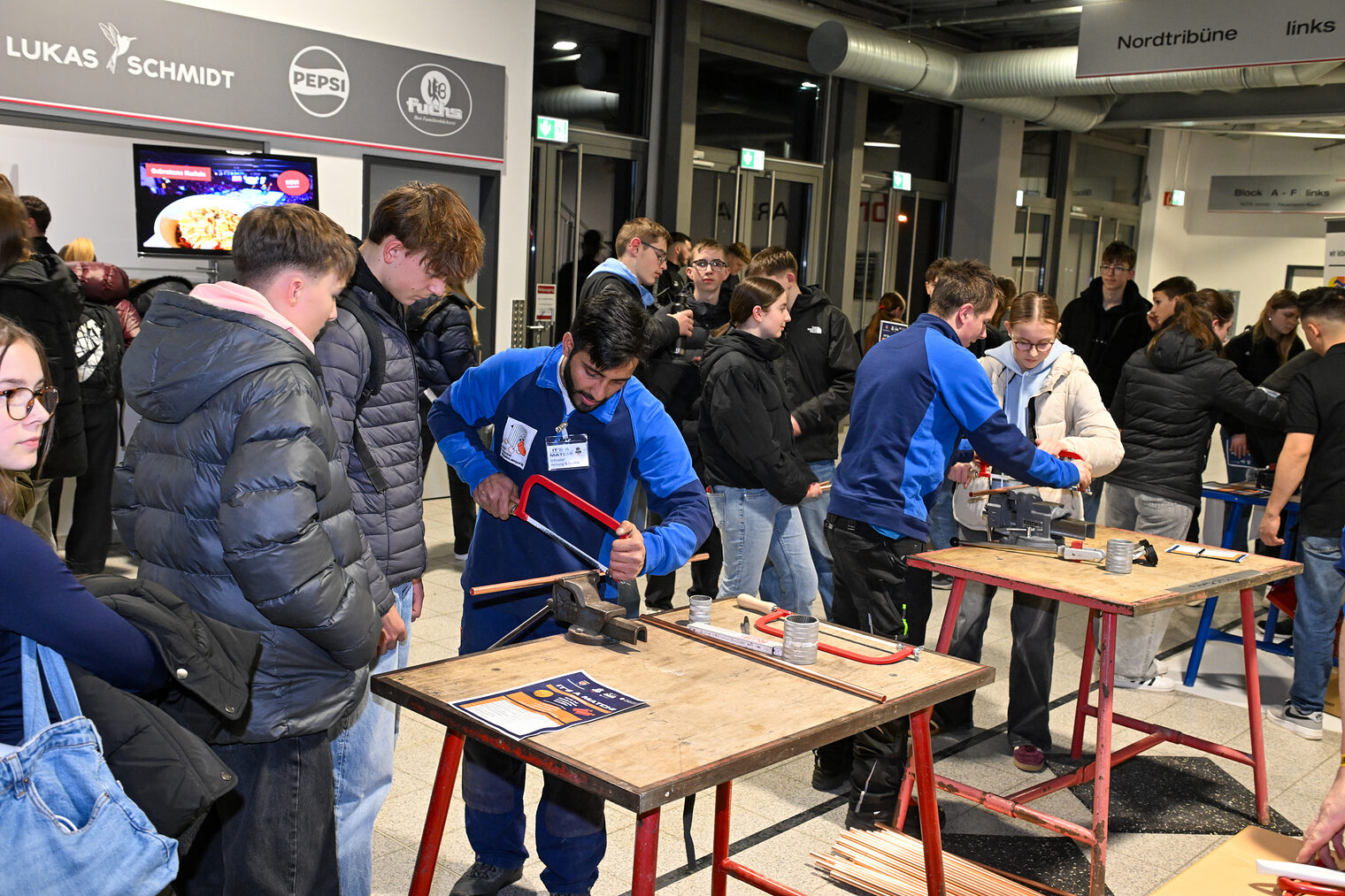 Schülerinnen und Schüler sägen Metallrohre mit Sägen zurecht.