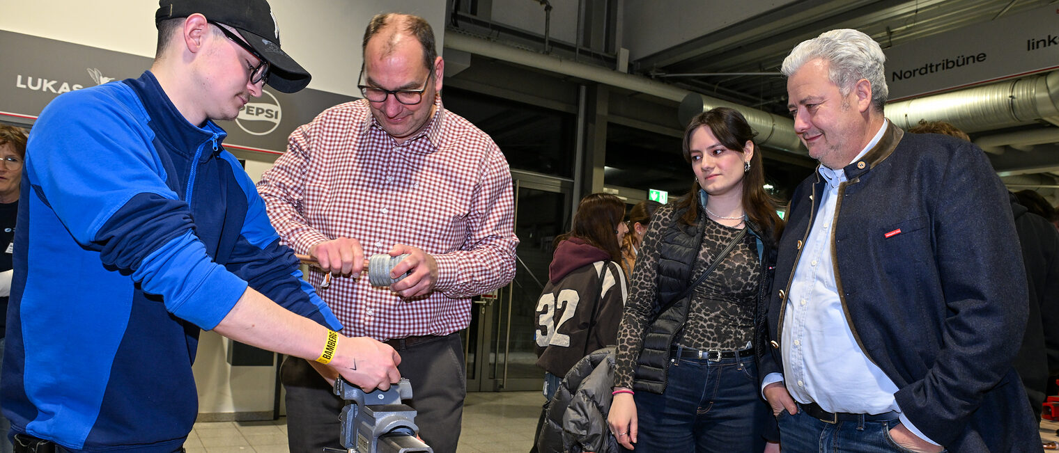 Ein Mann schleift an einem der Stände ein Metallrohr zurecht, während HWK-Präsident Matthias Graßmann zusieht.