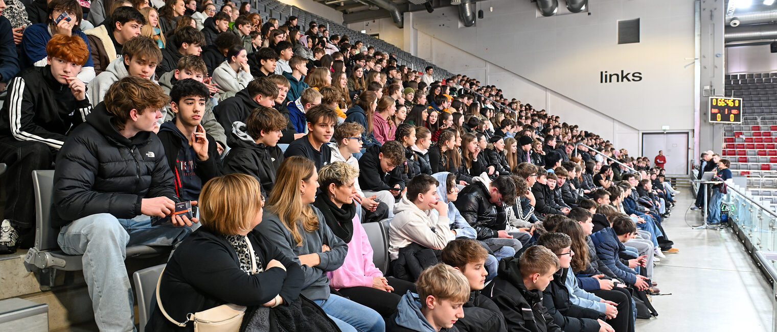 Die Schülerinnen und Schüler sitzen bei einem Vortrag auf der Nordtribüne.