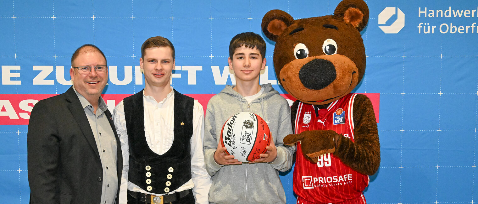HWK-Vorstandsmitglied Jens Beland, ein Vertreter von Holzbau Übel, ein Schüler mit dem Gewinnerball und Maskottchen Freaky
