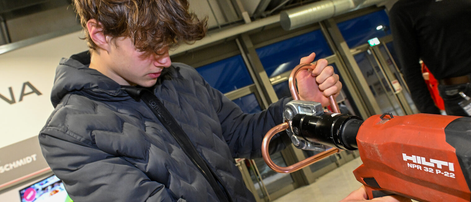 Ein Schüler biegt ein Herz aus Kupferrohren am Schraubstock zurecht.