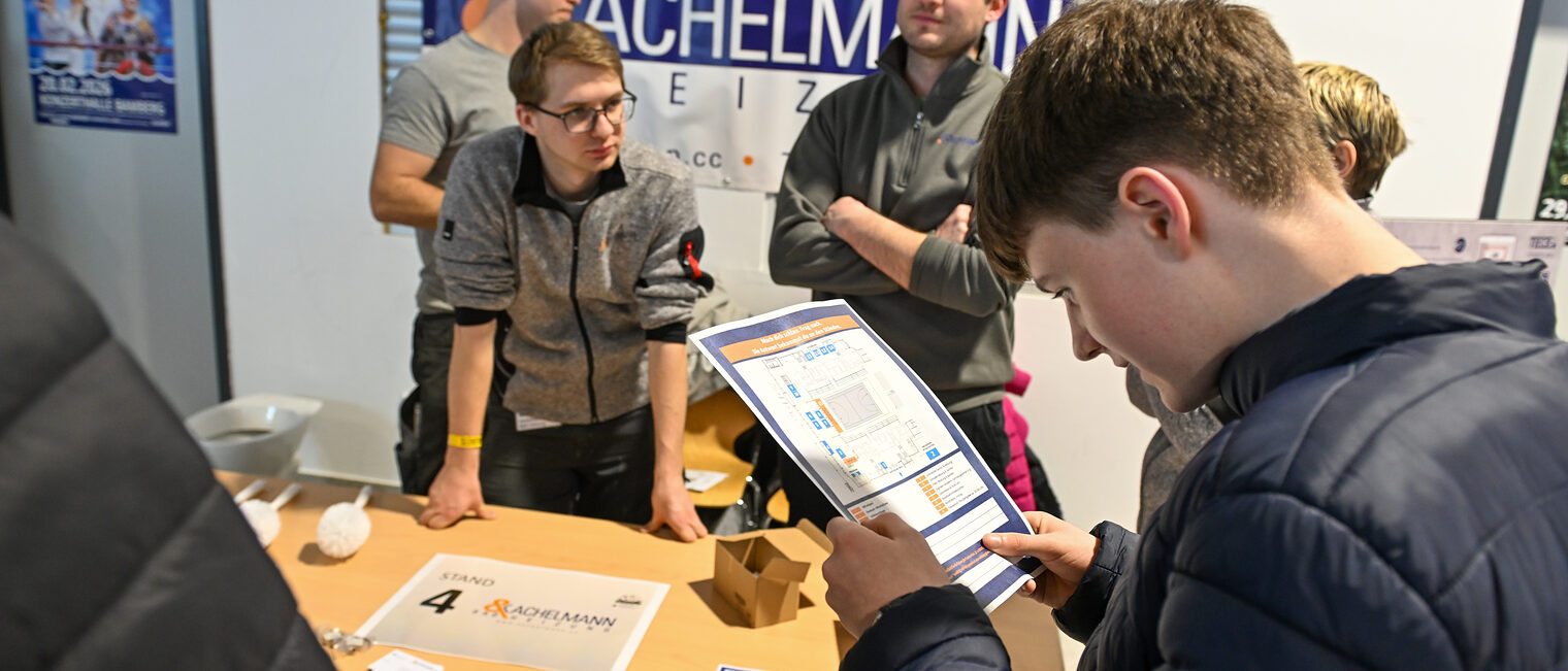 Ein Schüler füllt einen Zettel mit einem Quiz am Stand von Kachelmann Bad und Heizung aus.