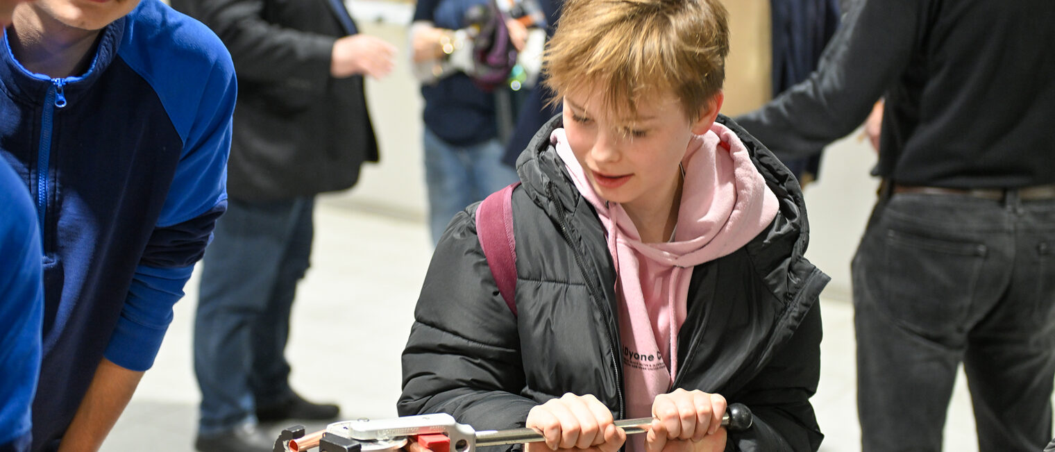 Ein Schüler biegt an einem Schraubstock ein Metallrohr zurecht.