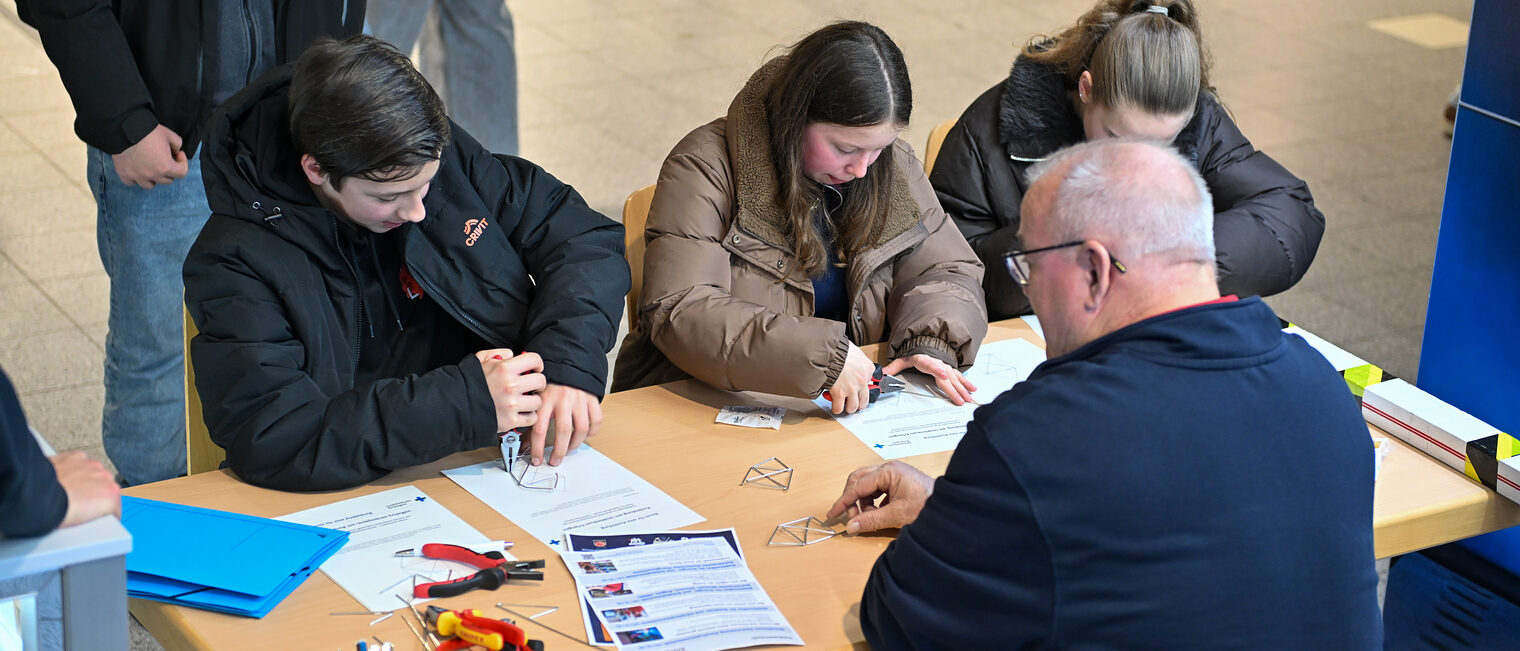 Schülerinnen und Schüler biegen Metalldrähte am Stand des Unicversitätsklinikums Erlangen zurecht.