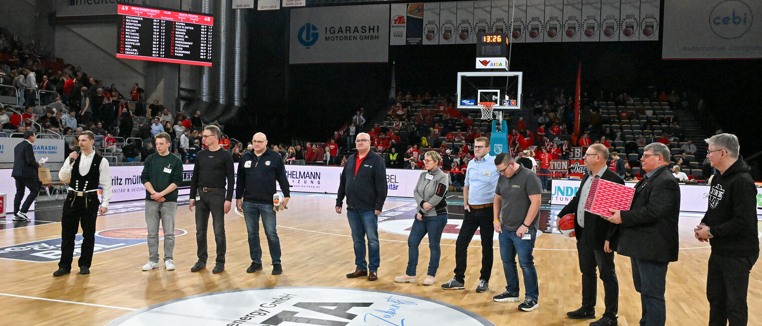 Die Vertreter der Betriebe stehen im Halbkreis auf dem Spielfeld der Brose-Arena.
