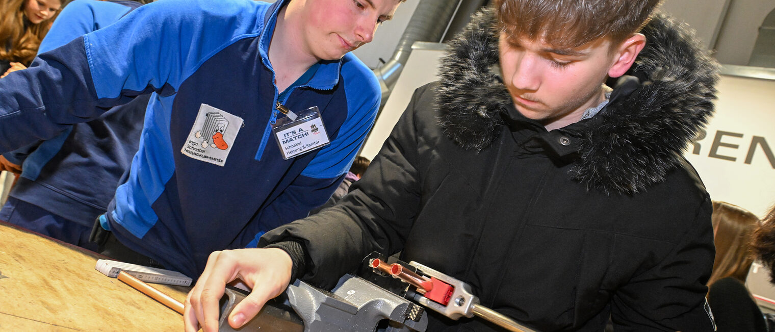 Ein Schüler biegt unter Aufsicht ein Kupferrohr an einem Schraubstock zurecht.