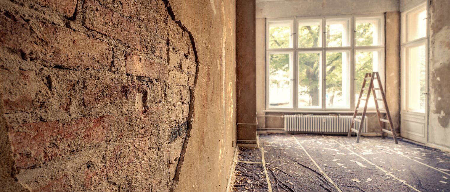 Eine Wand mit bröckelnden Putz legt eine Grundmauer frei.