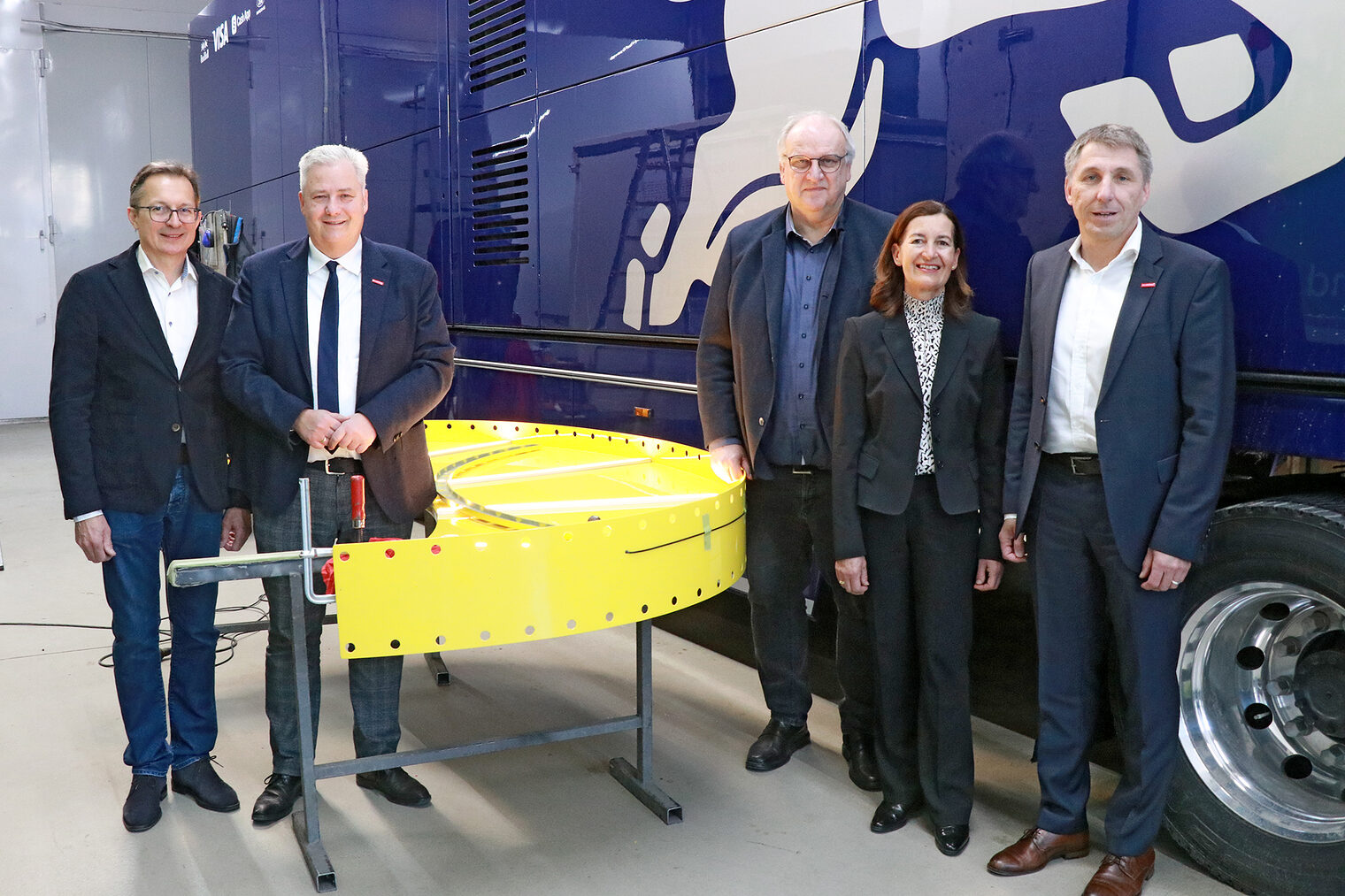 Peter Hofmann, Matthias Graßmann, Reinhard Bauer, Monika Hofmann und Rainer Beck stehen vor einem Renntruck und neben einem Anbauteil für Fahrzeuge. 