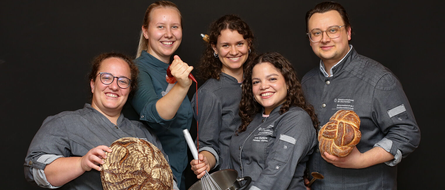 Die Meisterschülerinnen und -schüler für Bäcker und Konditoren posieren mit Arbeitsgegenständen. 