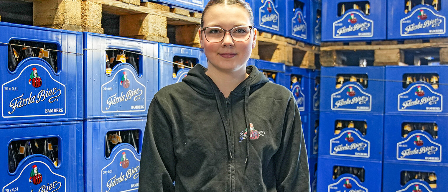 Lotta Trunk, Auszubildende zur Brauerin und Mälzerin steht vor aufgestapelten Bierkästen.