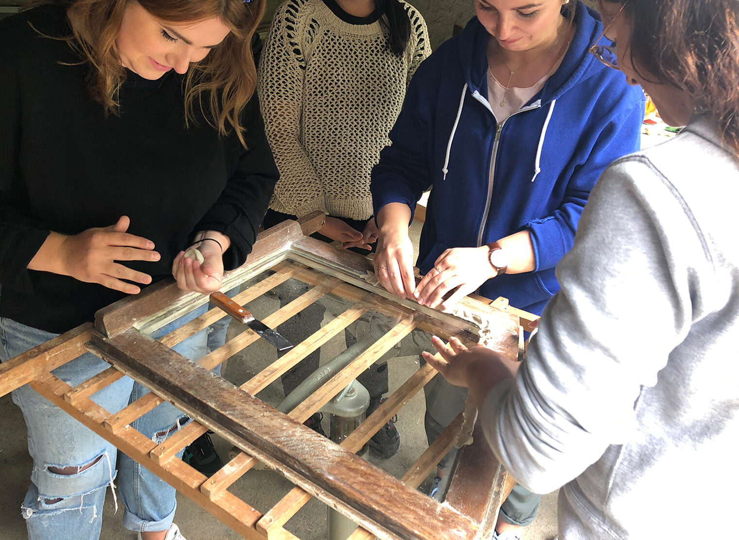 Eine Gruppe Studierender restauriert mit Werkzeug einen alten Fensterrahmen. 