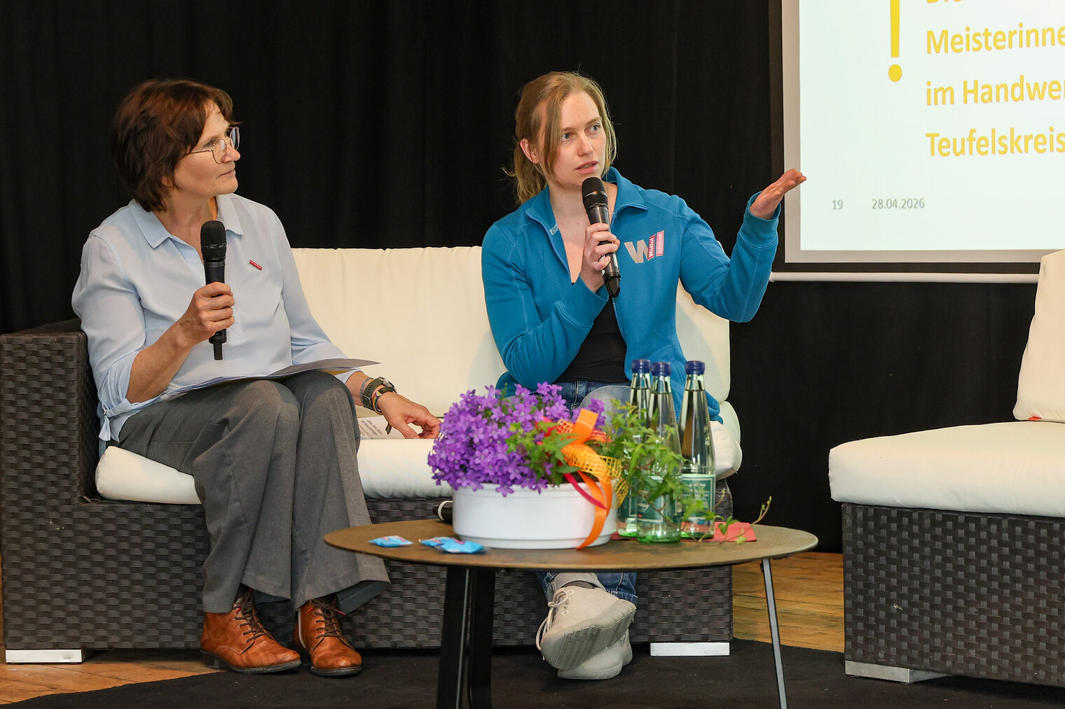 Michaela Heimpel und Tanja Wölfel sprechen auf einem Podium mit Mikrofonen miteinander.