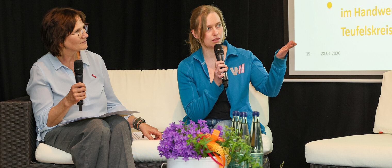 Michaela Heimpel und Tanja Wölfel sprechen auf einem Podium mit Mikrofonen miteinander.