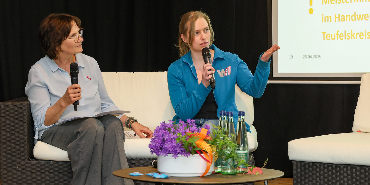 Michaela Heimpel und Tanja Wölfel sprechen auf einem Podium mit Mikrofonen miteinander.