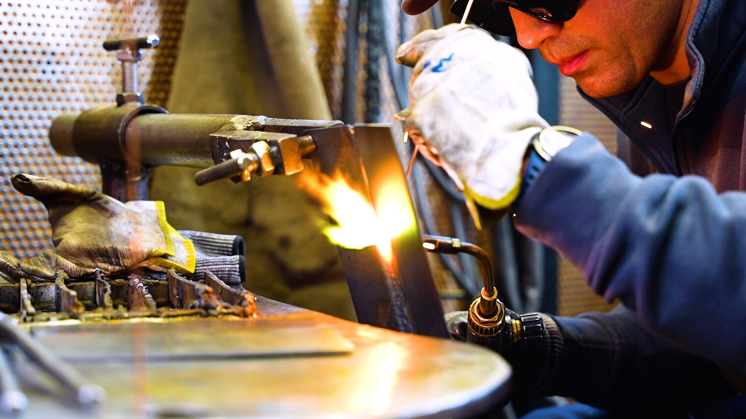 Ein Mann mit Schutzbrille schweißt Metallteile zusammen.