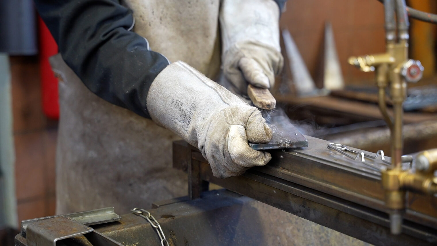 Ein Mann mit Schutzhandschuhen schleift ein Metallteil ab.