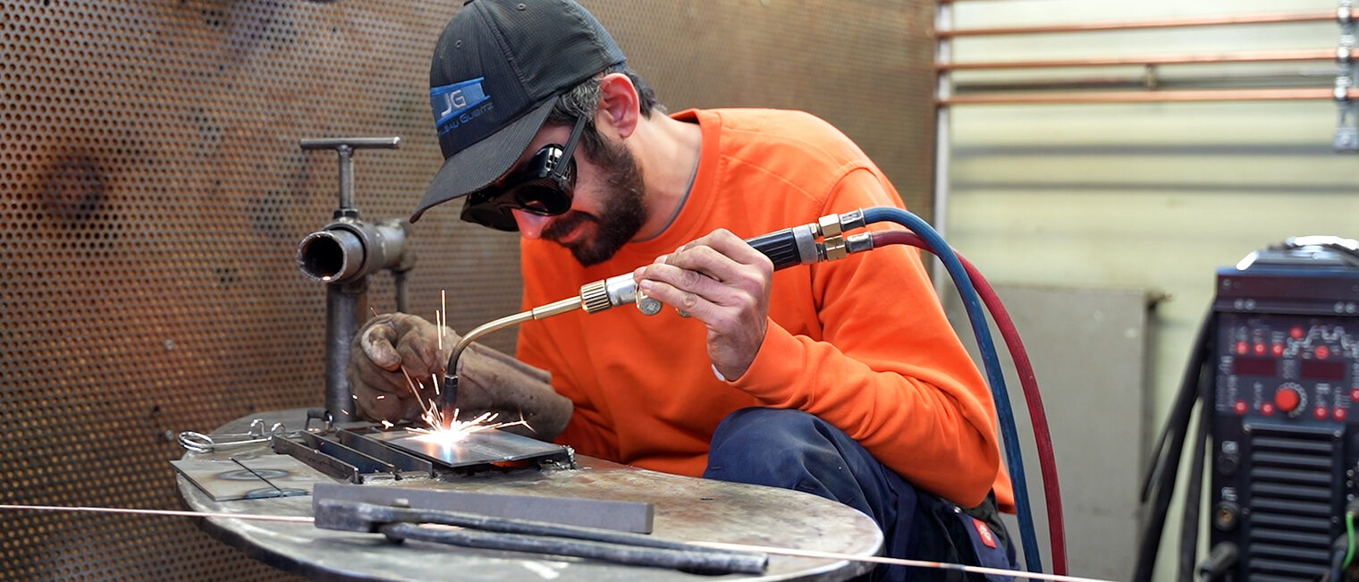 Ein Mann mit Schutzbrille schweißt zwei Metallteile zusammen.