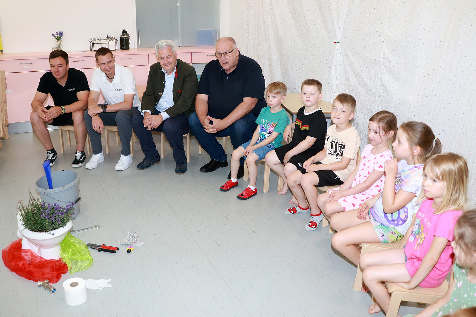 Stefan Gröger, Nico Bäuerlein, HWK-Präsident Graßmann, HWK-Hauptgeschäftsführer Reinhard Bauer und die Kinder der Kita Regenbogen sitzen auf kleinen Stühlen.