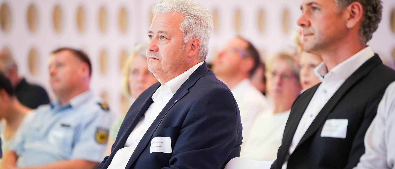 Matthias Graßmann und Dr. Schönberger hören einem Vortrag zu.