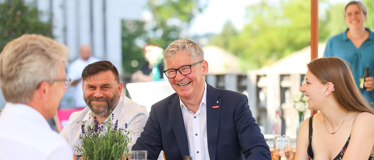 Christian Herpich und andere Gäste sitzen lachend an einem Tisch.
