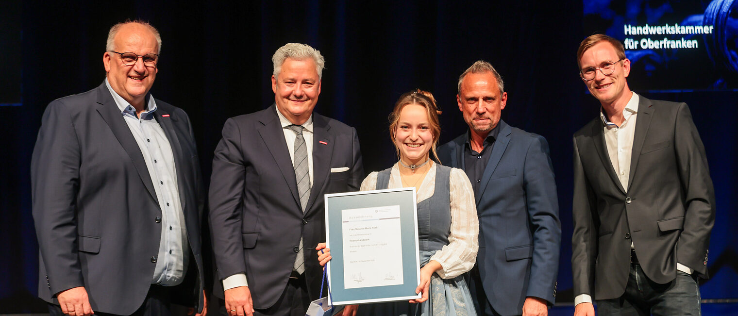 Jungmeisterin Melanie Marie Klaß präsentiert ihre Ehrenurkunde mit Gratulanten auf der Bühne.