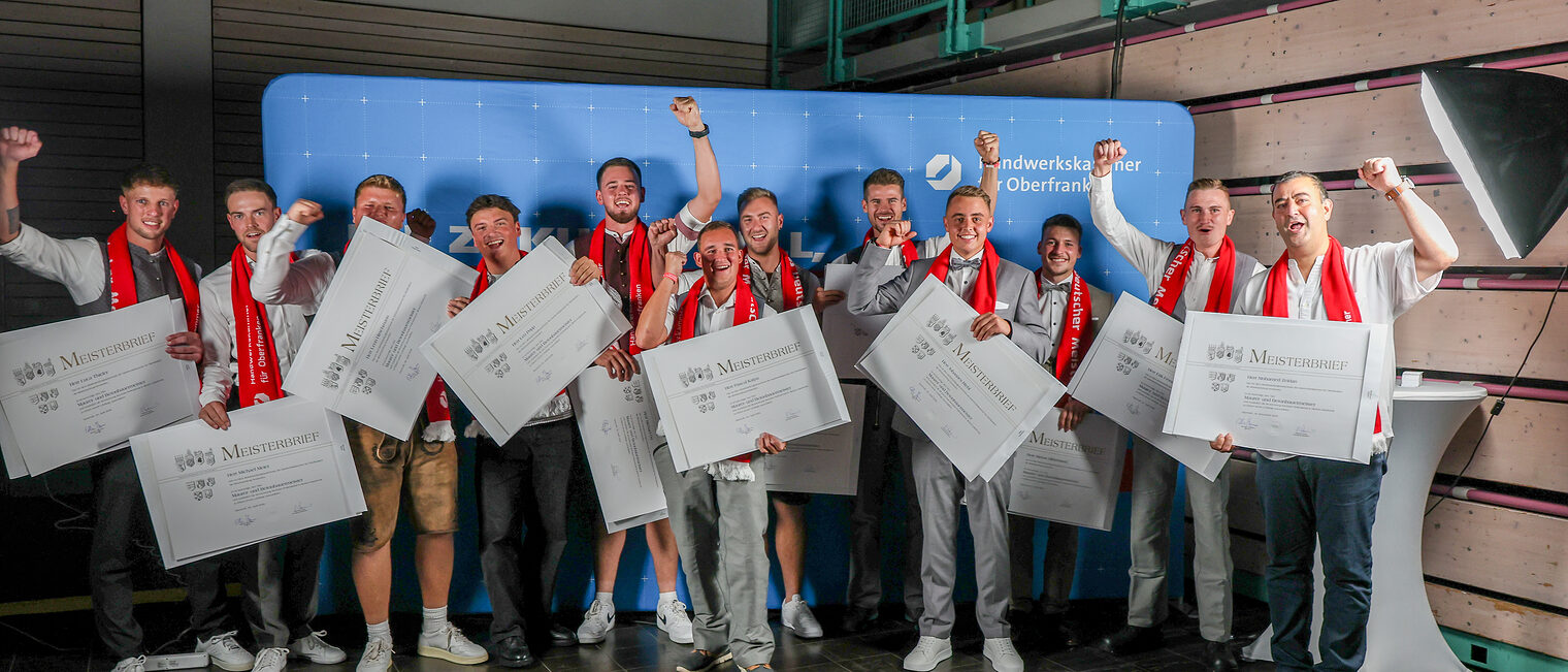 Die Jungmeisterinnen und Jungmeister im Maurer- und Betonbauermeisterhandwerk posieren für ein Gruppenfoto vor einer Fotowand.