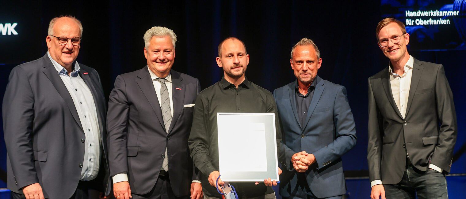 Ein Jungmeister präsentiert seine Ehrenurkunde mit Gratulanten auf der Bühne.