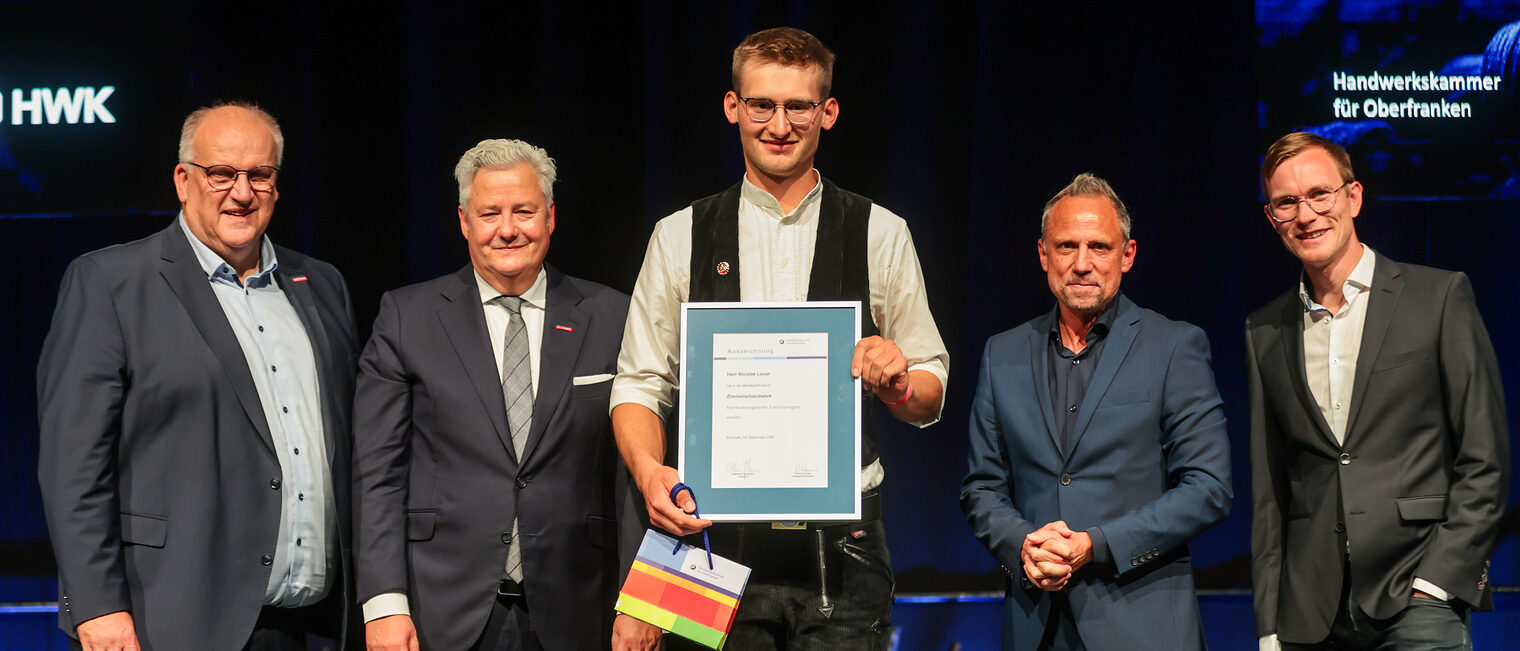 Jungmeister Nicolas Lauer präsentiert seine Ehrenurkunde mit Gratulanten auf der Bühne.
