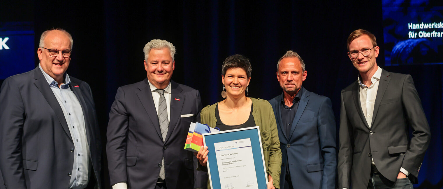 Jungmeisterin Tikvah Maria Wolff präsentiert ihre Ehrenurkunde mit Gratulanten auf der Bühne.