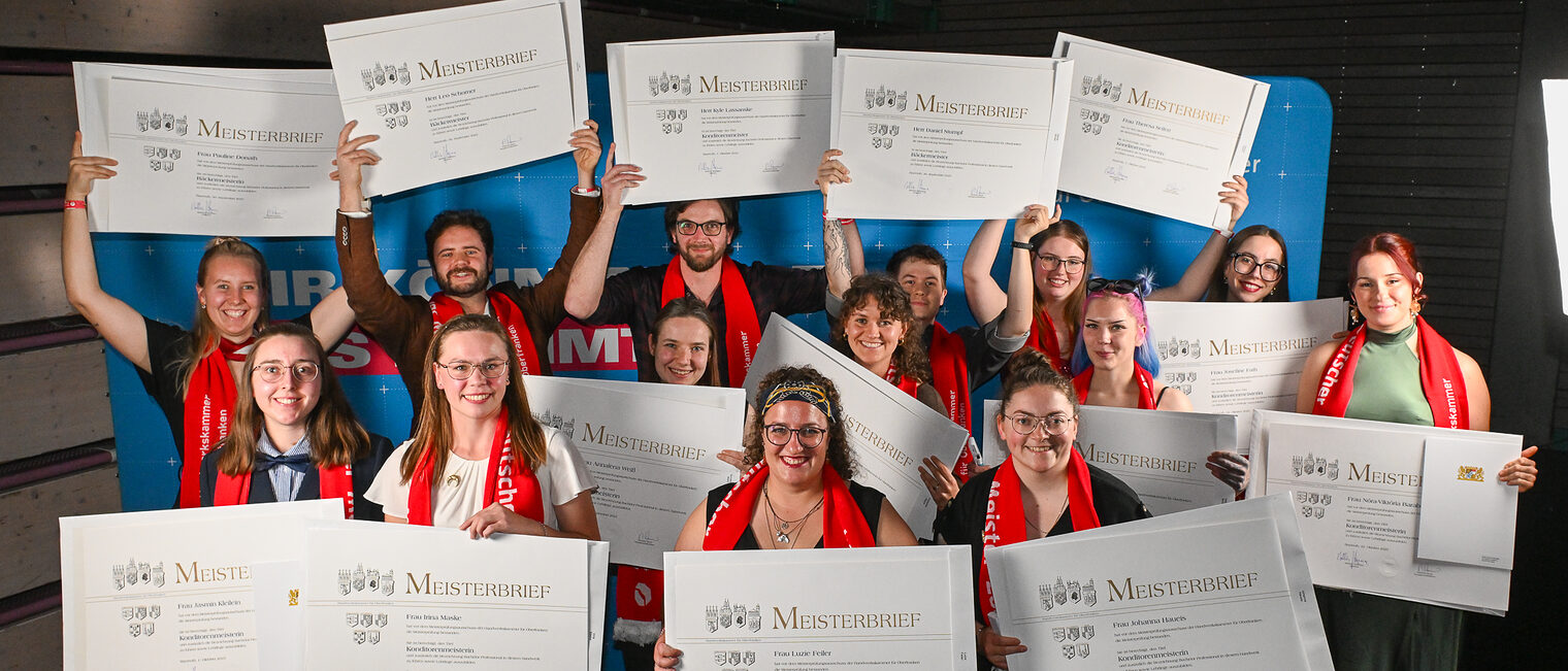 Die Jungmeisterinnen und Jungmeister im Bäcker- und Konditorenhandwerk posieren für ein Gruppenfoto vor einer Fotowand.