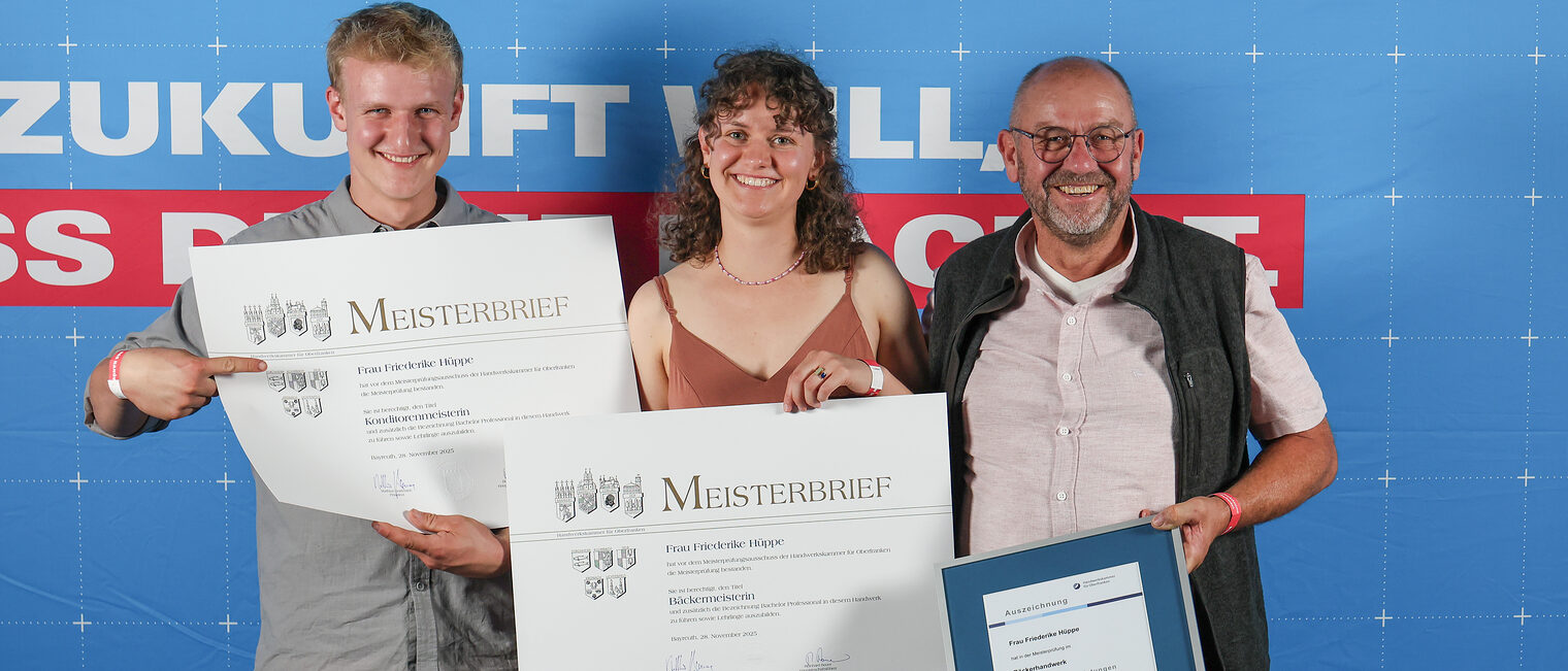 Jungmeisterin Friederike Hüppe posiert mit ihrer Familie vor einer Fotowand. 